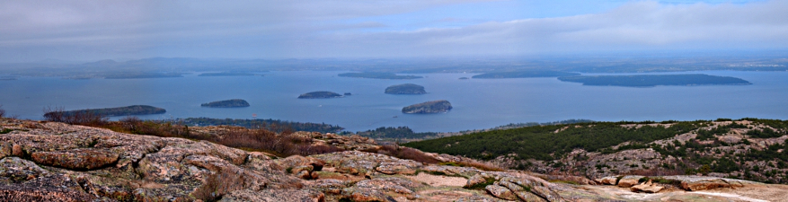 [Edge of Cadillac mountain in foreground and bay with many islands in background. Clouds in sky are visible.]